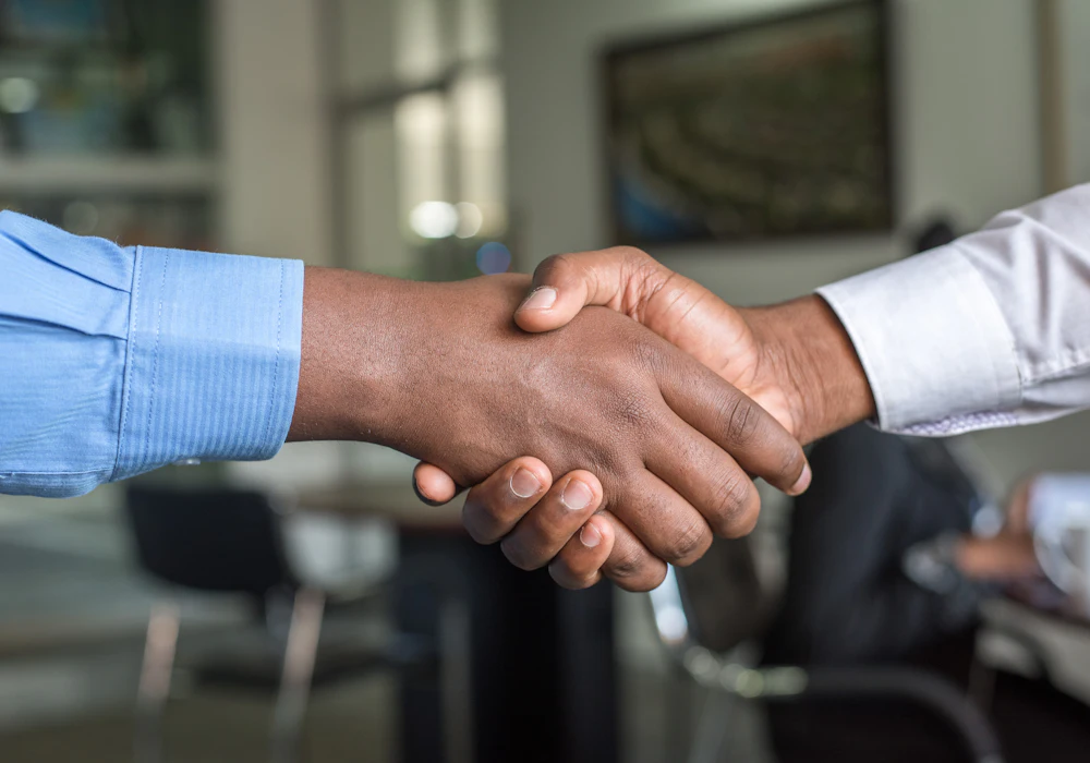 Two people shaking hands across a meeting table