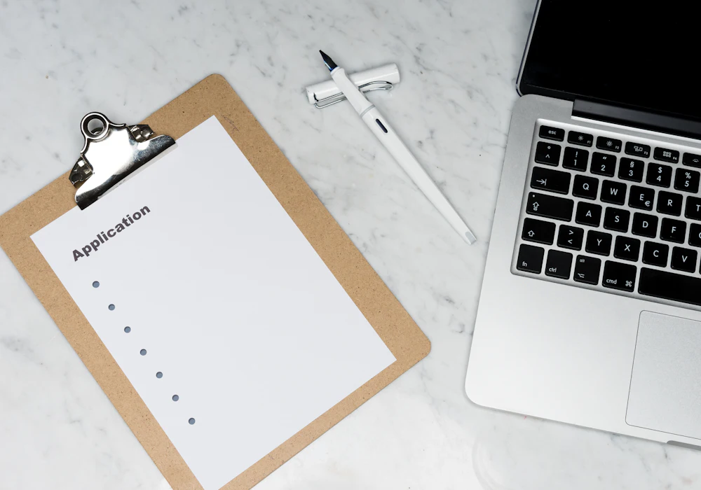 An application form on a clipboard beside a laptop